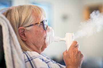 Senior lady breathing through oxygen inhaler at home. Medical and treatment concept.