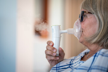 Senior lady breathing through oxygen inhaler at home. Medical and treatment concept.