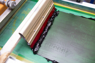 Serigraphy silk screen print process at clothes factory. Frame, squeegee and plastisol color paints.