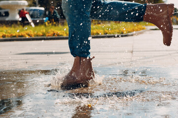 Woman wearing rain rubber boots walking running and jumping into puddle with water splash and drops in autumn rain.