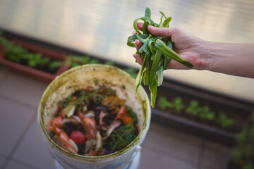 A hand of a woman throws cucumber peels into the compost on her apartment balcony.
