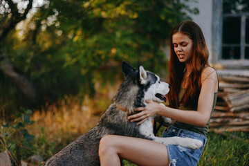 Joyful woman with a husky breed dog smiles while sitting in nature on a walk with a dog on a leash autumn landscape on the background. Lifestyle in walks with pets