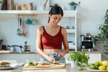 Healthy young woman cutting fresh vegetables while cooking healthy food in the kitchen at home.