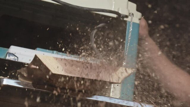 Closeup of a man carpenter working with a thickness planer. Dust flying out during the wood processing