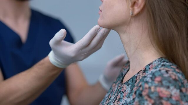 Close-up doctor hand touching chin of unrecognizable patient in plastic surgery clinic. Professional Middle Eastern surgeon in gloves examining imperfections and face shape of Caucasian woman