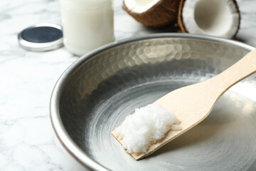 Frying pan with coconut oil and wooden spatula on white marble table, closeup. Healthy cooking