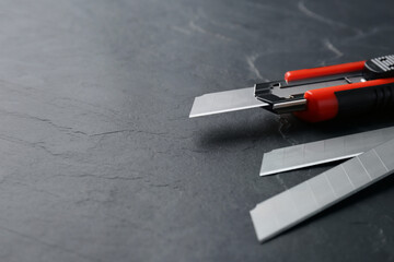 Utility knife and blades on black table. Space for text