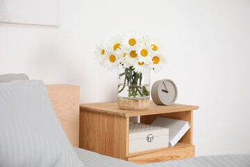 Bouquet of beautiful daisy flowers on wooden nightstand in bedroom
