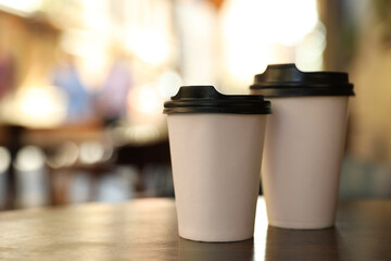 Cardboard takeaway coffee cups with plastic lids on wooden table in outdoor cafe, space for text