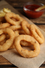 Delicious onion rings, fries and ketchup on wooden table, closeup