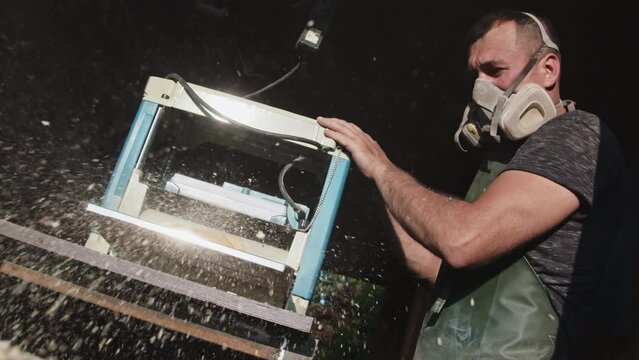 A man works with a thickness planer. Carpenter trimming a board using a personal protective. Dust flying out during the wood processing