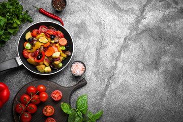 Frying pan with tasty cooked vegetables and fresh ingredients on grey table, flat lay. Space for...