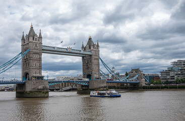 London, England, UK - July 6, 2022: Tower bridge seen from Tower of London quay under heavy cloudscape. Boats on brown Thames and traffic on bridge.