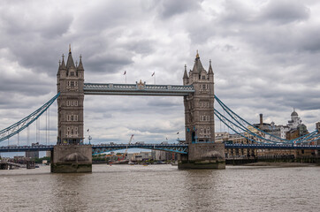 Fototapeta na wymiar London, England, UK - July 6, 2022: Tower bridge seen from up brown water Thames on Western side under thick gray cloudscape.
