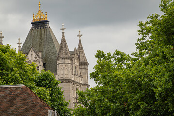 London, England, UK - July 6, 2022: Golden crown on Tower bridge North Tower seen from Tower of London under gray sky with green foliage on sides. 