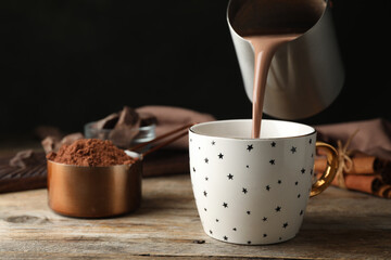 Pouring hot cocoa drink into cup on wooden table