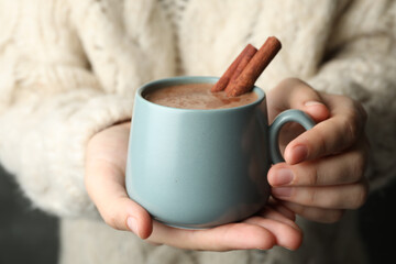 Woman holding cup of delicious hot cocoa with cinnamon, closeup