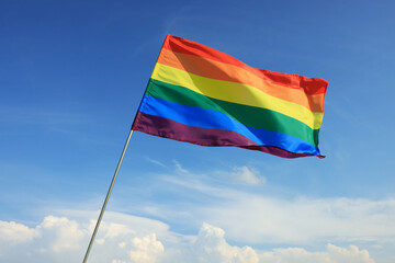 Woman holding bright LGBT flag against blue sky, closeup