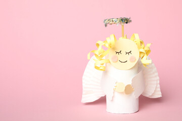 Toy angel made of toilet paper hub on pink background. Space for text