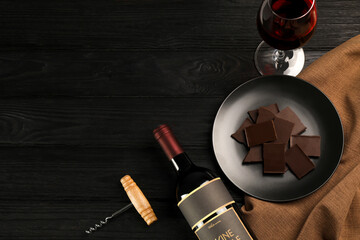 Flat lay composition with tasty red wine and chocolate on black wooden table. Space for text