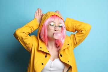 Fashionable young woman in pink wig with bright makeup blowing bubblegum on yellow background