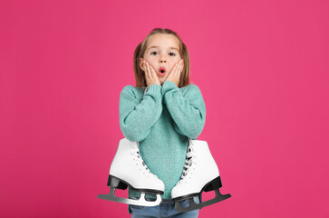 Excited little girl in turquoise knitted sweater with skates on pink background