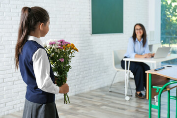 Schoolgirl with bouquet congratulating her pedagogue in classroom. Teacher's day