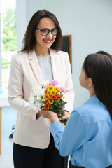 Schoolgirl congratulating her pedagogue with bouquet in classroom. Teacher's day