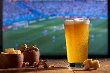 watching the soccer on a large TV with a glass of beer, peanuts and cheese
