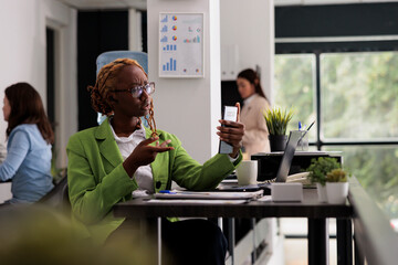 Employee talking on smartphone video call in coworking space, having videoconference in start up business office. Manager chatting on mobile phone teleconference at workplace desk