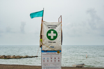 A lifeguard chair on Toronto's Woodbine Beach flies a green flag indicating good conditions; little to no waves and off-shore wind. Shot on a rainy afternoon in August. Room for text.