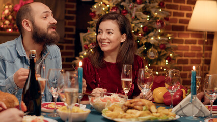 Festive married couple enjoying chatting with relatives while sitting at Christmas dinner table....