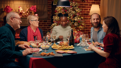 Cheerful diverse family enjoying Christmas dinner at home while eating traditional home cooked...