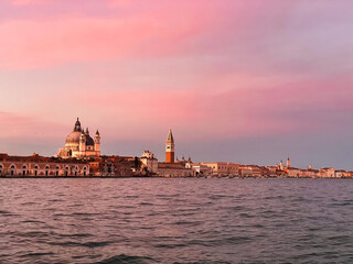 Dramatic sunset with pink sky over Venice from boat, looking over the water towards the Basilica and St Mark's Square 