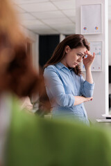 Fototapeta premium Depressed employee having professional burnout, suffering from headache at work, touching forehead, exhausted woman in coworking space. Frustrated person with migraine feeling unwell at workplace