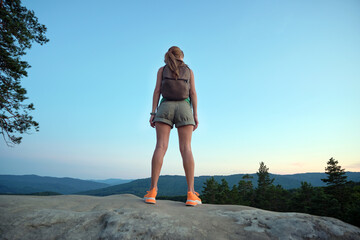 Young woman hiker standing alone on mountain footpath enjoying view of evening nature on wilderness trail. Active way of life concept