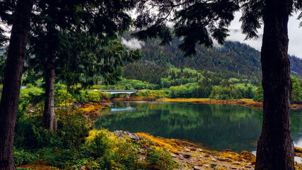 Trees and bridge reflected in placid waters of Skidegate Inlet from Bearskin Bay, Haida Gwaii, BC,...