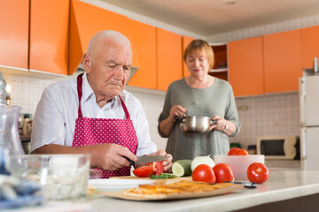 Happy elderly man and woman making dinner together in kitchen