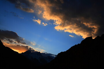 Obraz premium Dramatic sunset and golden sunrays emanating from behind the peaks around Boroghil valley national park in Pakistan. 