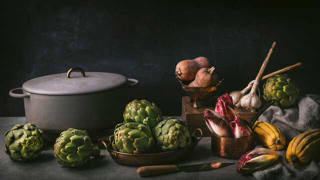 Moody front shot still life arrangement of artichokes, red endive, garlic and winter squash. Inspired by Dutch still life paintings
