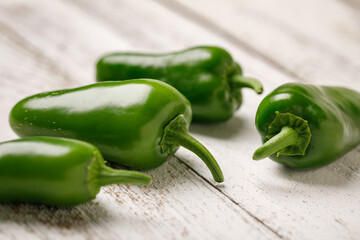 Whole green organically homegrown jalapeno peppers on a white washed wooden background
