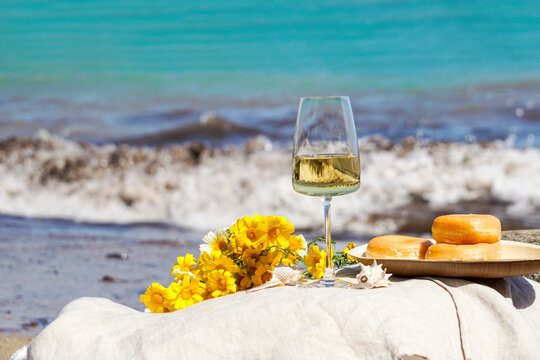 glass with white wine on stone stools against blue sea and waves, summer picnic concept