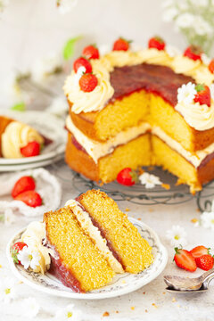 A slice of custard flavoured sponge cake filled with jam and cream on a small plate. The whole cake is in the background.
