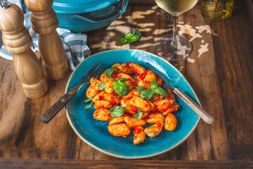 Traditional Italian potato Gnocchi with tomato sauce and fresh basil on blue plate on wooden background.