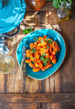 Traditional Italian potato Gnocchi with tomato sauce and fresh basil on blue plate on wooden background.