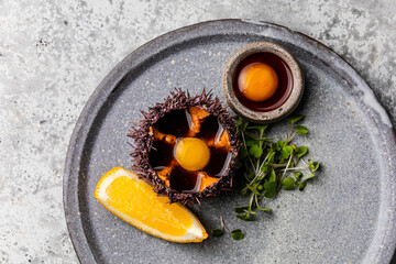 Fresh opened Sea Urchin with quail egg and soy sauce on plate on gray background