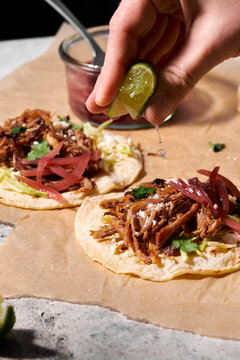 A hand squeezing a lime over pork tacos with pickled red onions.
