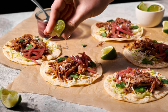 A hand squeezing a lime over pork tacos with pickled red onions.