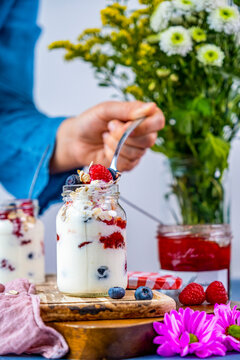 Woman taking a spoonful of yogurt from a small jar filled with yogurt breakfast parfait