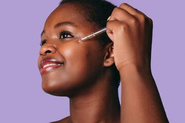 Portrait of beautiful black afro woman applying organic essential serum on face with pipette...
